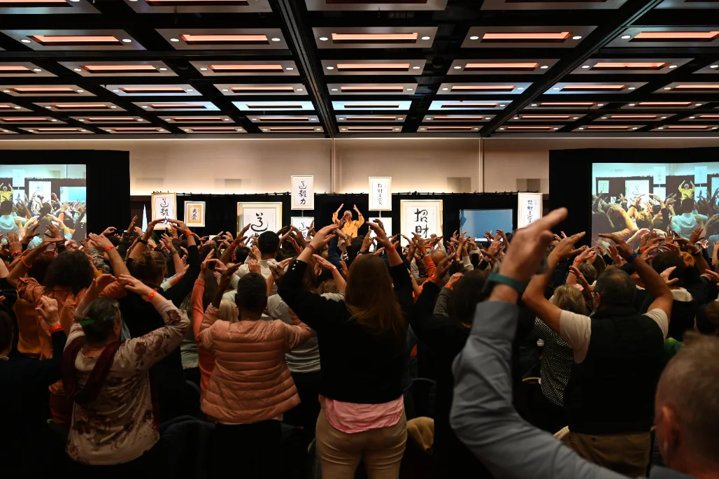 Dr. and Master Sha teaching a live workshop to a full audience with hands raised
